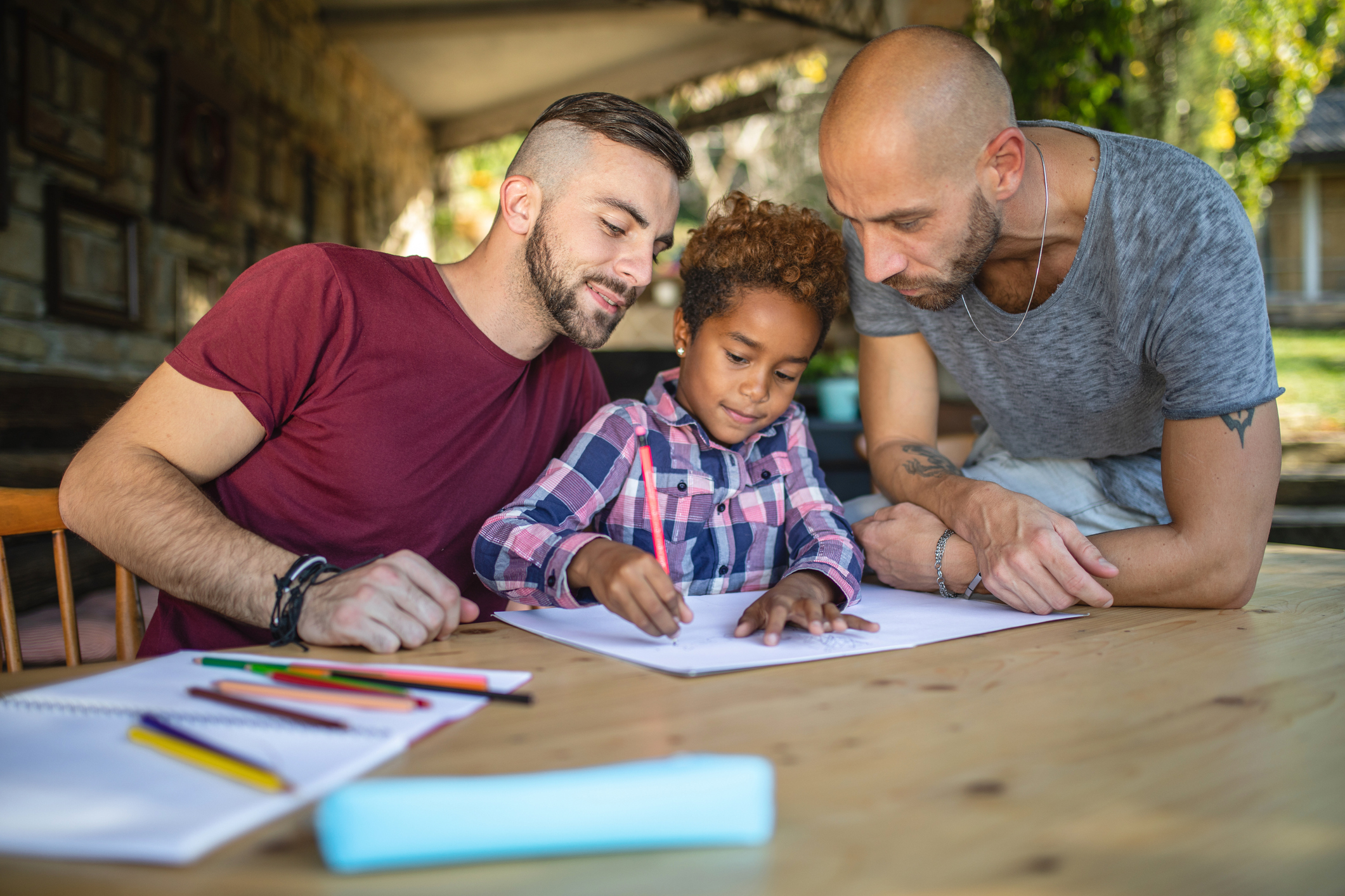 Lovely gay couple doing homework with their adopted daughter